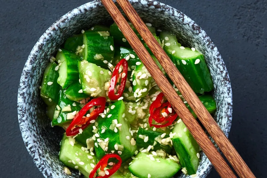 Top-down bowl of spicy cucumber salad with sesame seeds and red chile