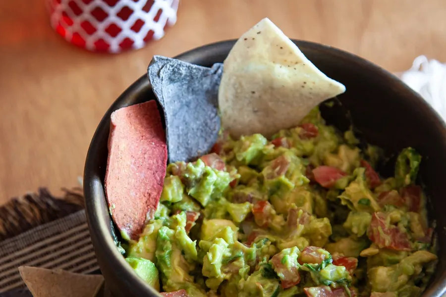 Bowl of guacamole with tortilla chips on a wooden table