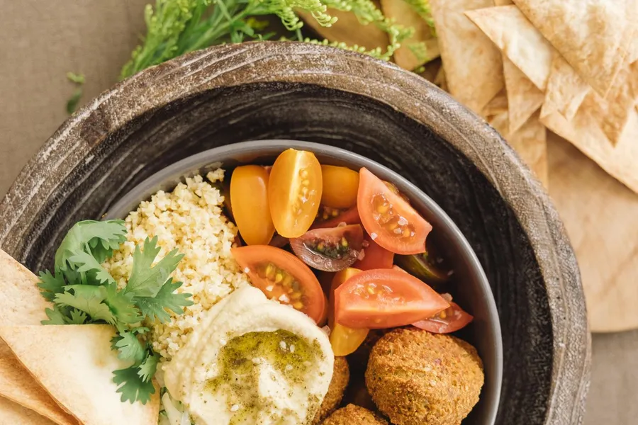 Top-down Mediterranean grain bowl with couscous, falafel, hummus, cucumbers, tomatoes, and pita