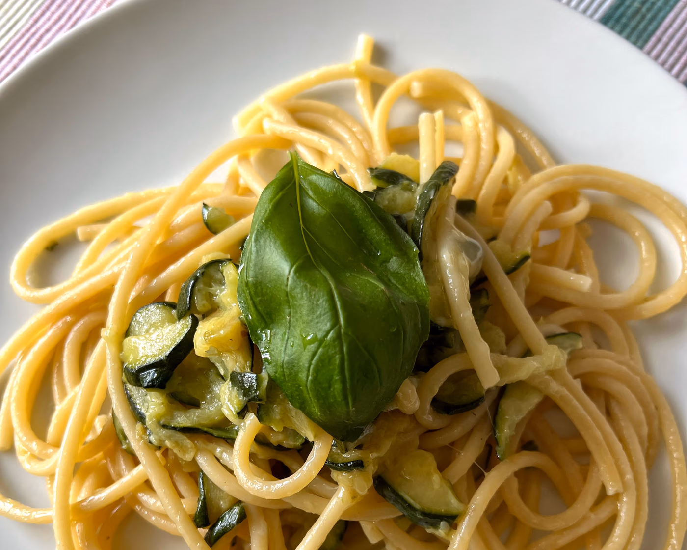 Plate of spaghetti with zucchini and basil on a white plate